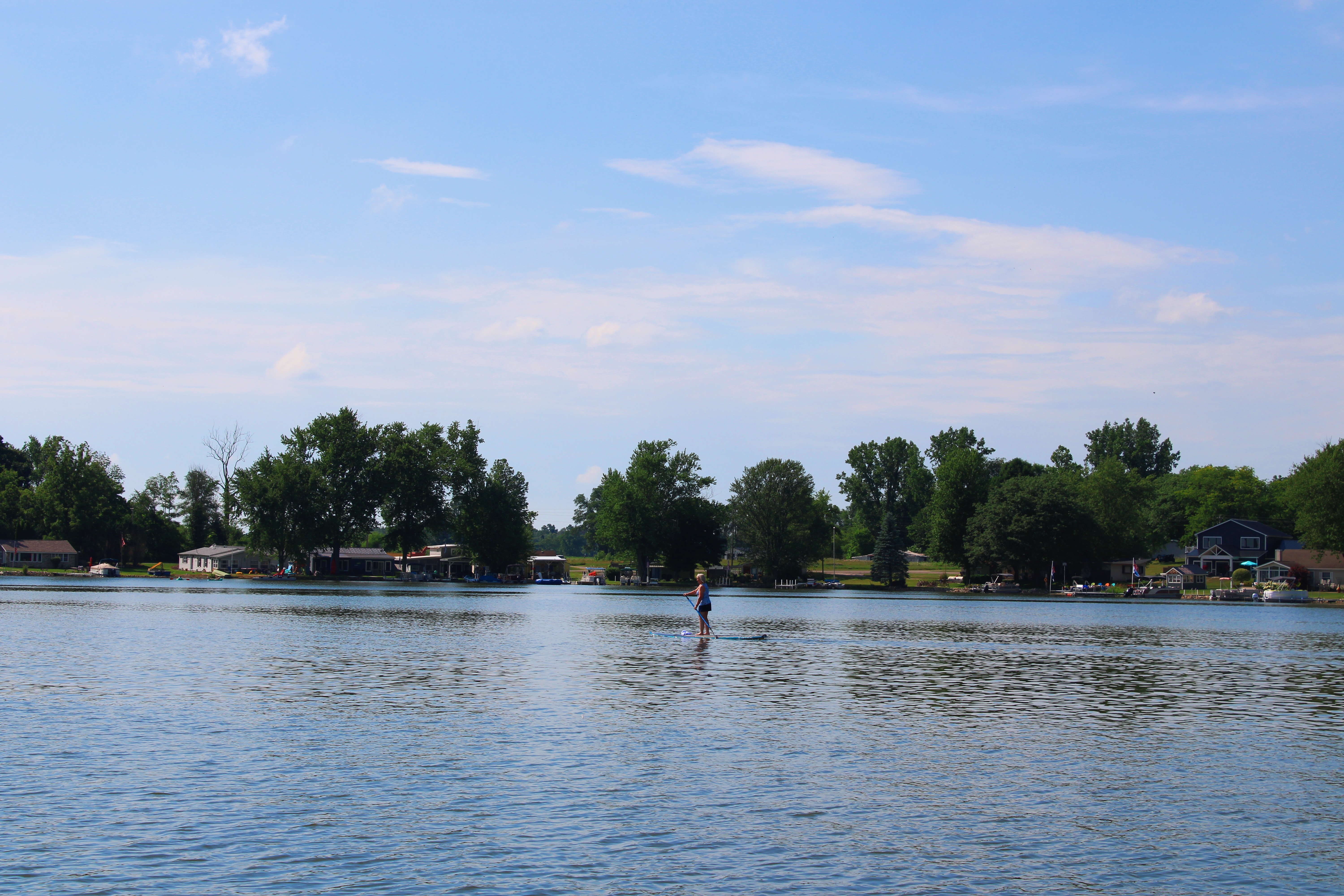 A woman enjoys paddleboarding on a tranquil Indiana lake, reflecting the clear blue sky above.