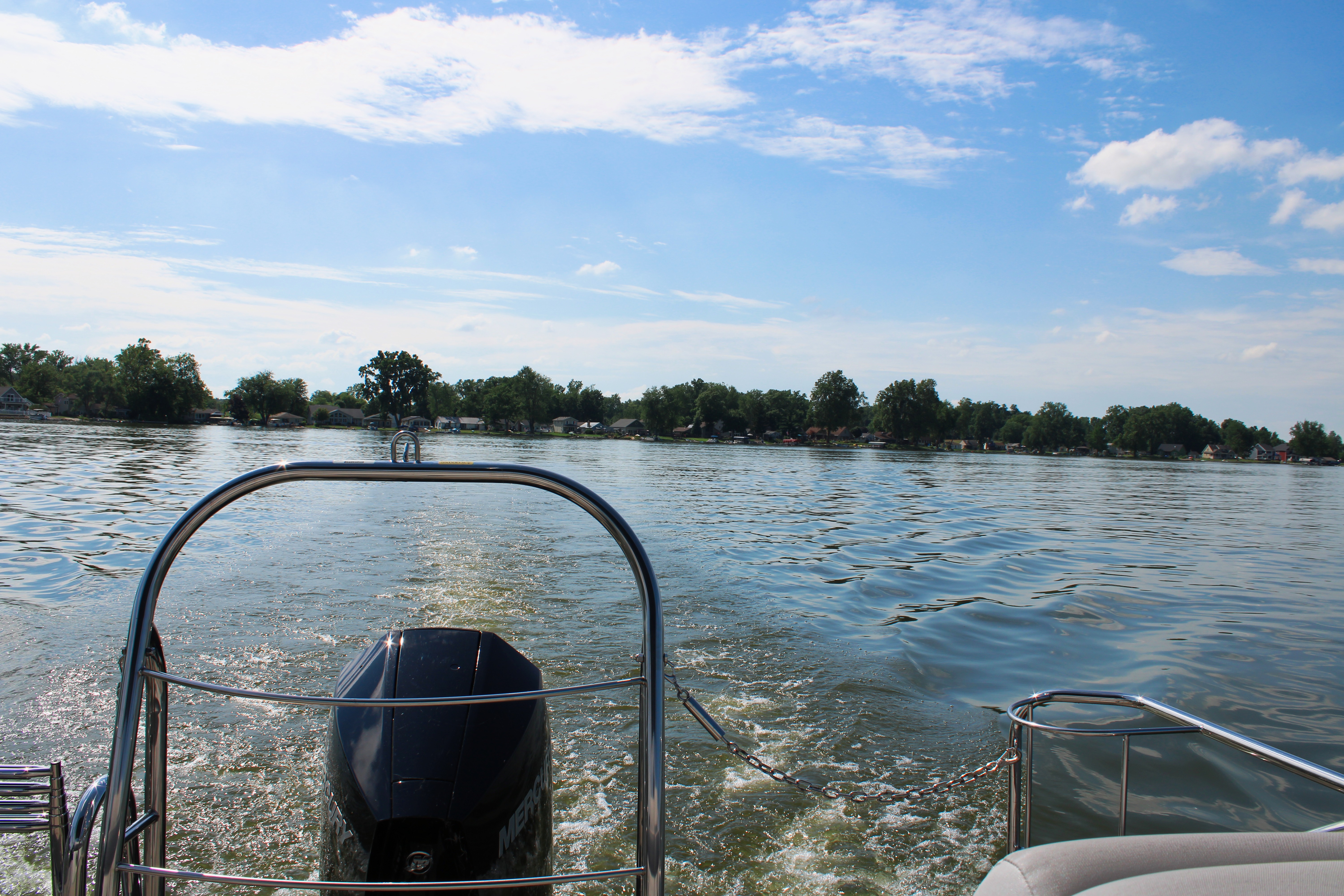 A view of a pontoon boat on a lake, creating a wake as it moves through the water.